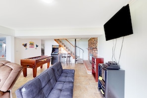 Ein Wohnzimmer mit Tischfußball, einer Couch, einem Fernseher und einer Treppe, die in einen Küchenbereich führt.