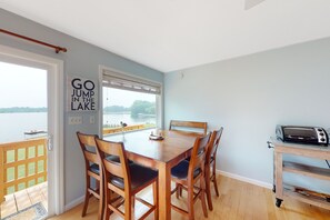 Ein Essbereich mit Seeblick, einem Holztisch, vier Stühlen, einem Toaster und einem Schild mit der Aufschrift 'GO JUMP IN THE LAKE'.