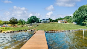 A wooden dock leading to a pond with a house in the background. - Charming Getaway With a Fireplace, Large Deck, Paddle Boards & Porch Swing (Mineral)