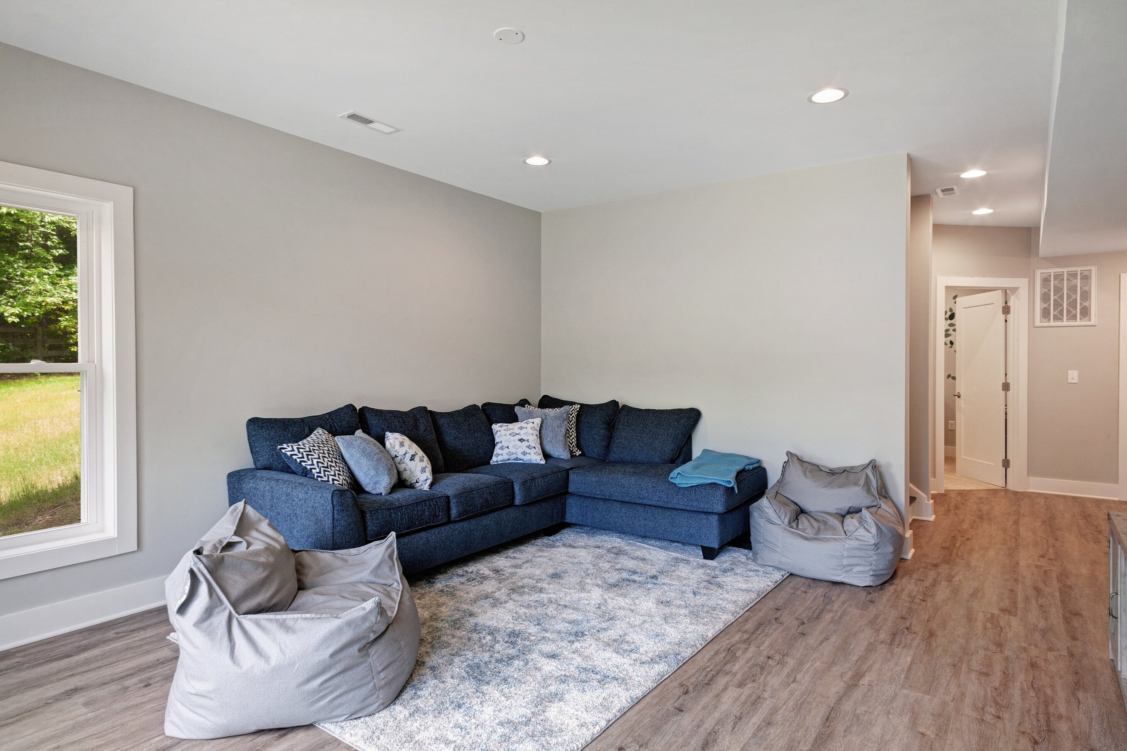 A modern living room with a sectional sofa, a large rug, and a view of a green outdoor area.