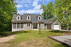 A two-story house with a front porch, a garage, and a small yard. - Custom Lakefront Home With Private Beach, Dock & Firepitq (Bumpass)