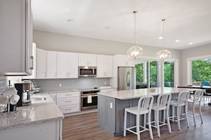 A modern kitchen with white cabinets, stainless steel appliances, and a large island with bar stools. - Custom Lakefront Home With Private Beach, Dock & Firepitq (Bumpass)