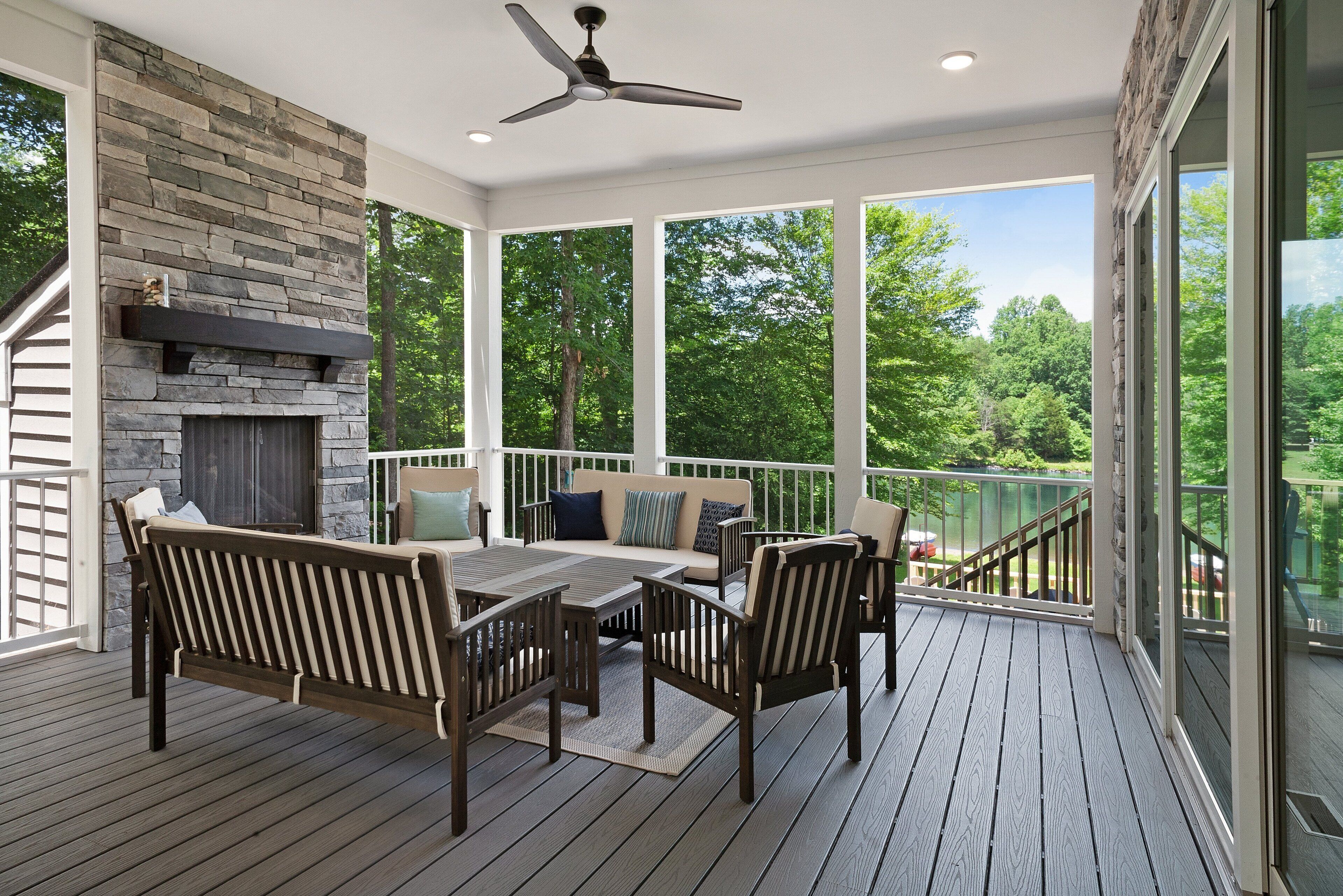 A covered outdoor area with a stone fireplace, wooden furniture, and a view of the surrounding trees.
