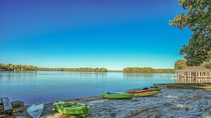 Un lago tranquillo con kayak sulla riva, un gazebo e un cielo azzurro limpido.