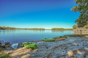 Ein ruhiger See mit Kajaks am Ufer, einem Pavillon und blauem Himmel.