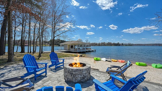 Una terrazza sul lago con poltrone Adirondack blu, un braciere in pietra e un pontile che si protende sull'acqua.