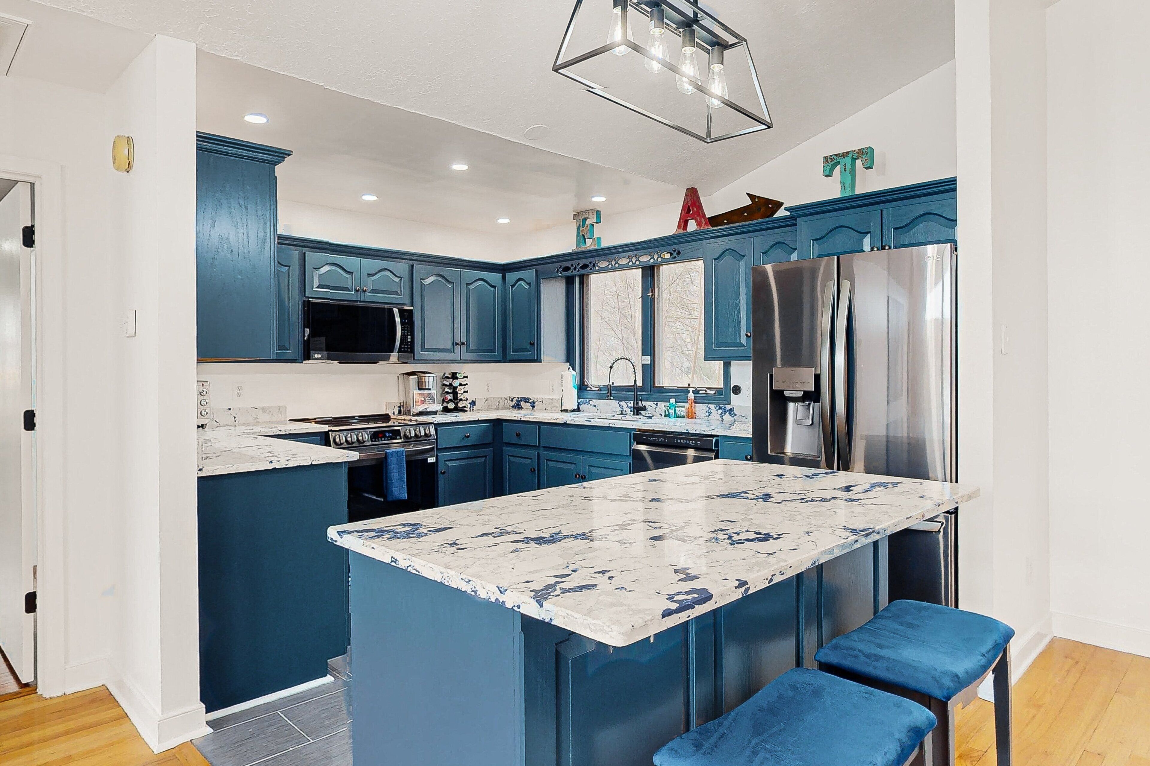 A modern kitchen with blue cabinetry, a large island, stainless steel appliances, and a pendant light.