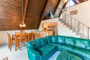 A loft-style living space with a wooden ceiling, a green leather sofa, a dining area, and a kitchen. - Charming, Lakefront A-frame With Private Dock, Lakeside Gazebo, Spacious Deck (Bumpass)