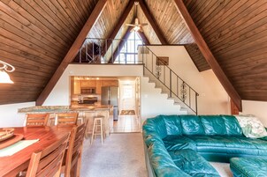 Un espacio tipo loft con zona de comedor, un sofá de cuero verde, una escalera y una cocina al fondo.