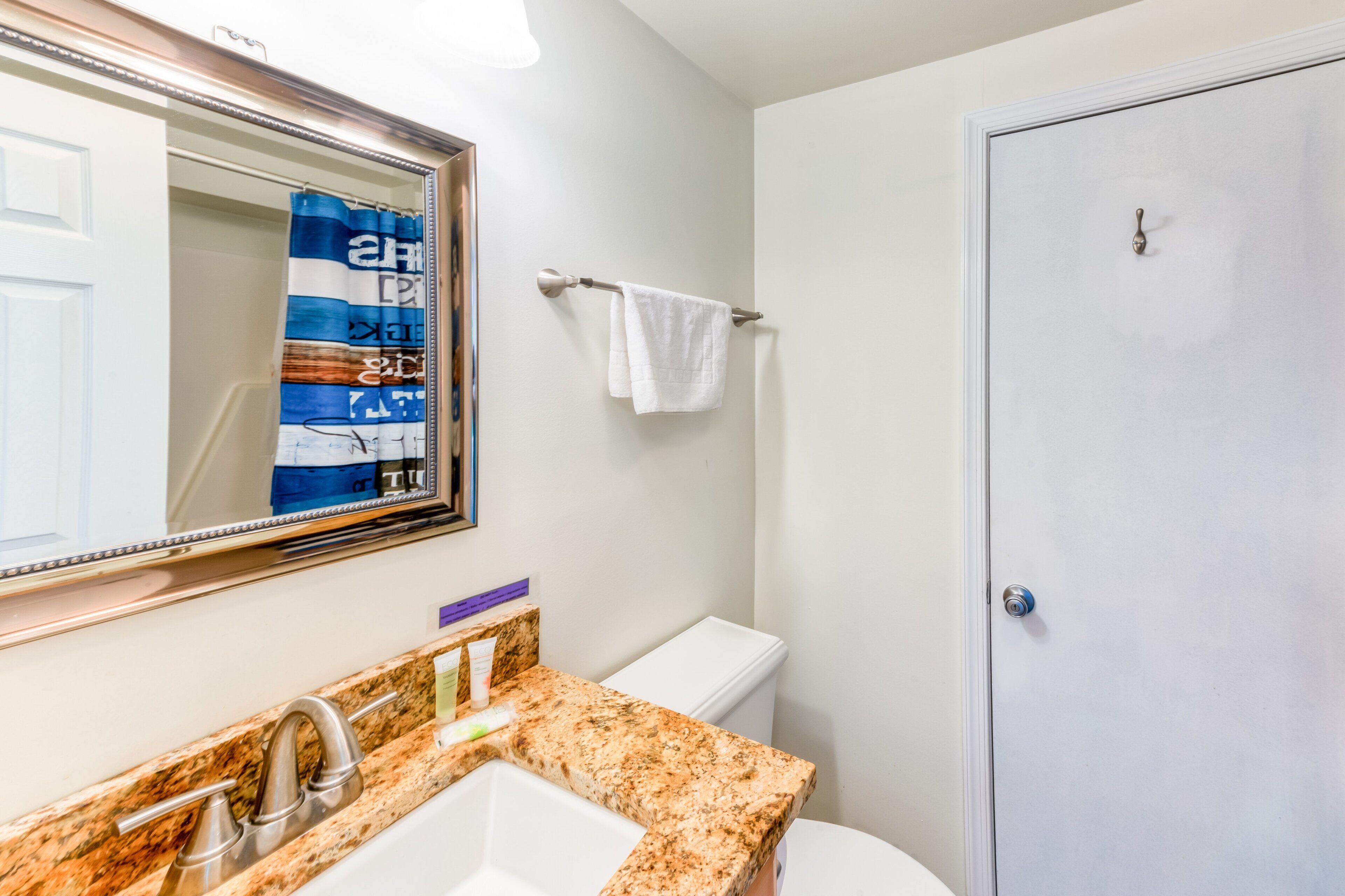 A bathroom with a granite countertop, a white sink, a mirror, a towel rack, and a toilet.