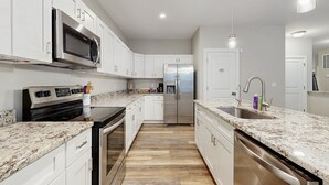 A modern kitchen with white cabinets, stainless steel appliances, a granite countertop, and a wooden floor. - Cozy Retreat With Forest Views, Peaceful Vibes & Modern Comfort (Bumpass)