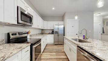 A modern kitchen with white cabinets, stainless steel appliances, a granite countertop, and a wooden floor.