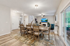 A dining area with a wooden table and chairs, a fireplace, a television, and a view of the outdoors. - Cozy Retreat With Forest Views, Peaceful Vibes & Modern Comfort (Bumpass)