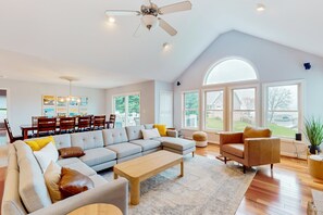 A spacious living room with a sectional sofa, a coffee table, a fireplace, and large windows offering a view of the outdoors. - Dog-friendly Lake Luxury With dry Sauna, hot Tub, Game Room (Bumpass)