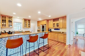 A modern kitchen with wooden cabinets, a central island with bar stools, and a large window. - Dog-friendly Lake Luxury With dry Sauna, hot Tub, Game Room (Bumpass)