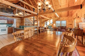 A spacious wooden dining area with a large table and chairs, a kitchen with wooden cabinets, and a staircase leading to an upper level. - Dog-friendly, Lake View Cabin w/ Furnished Decks, Ping-pong & Darts (Louisa)