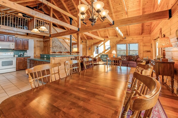 A spacious wooden dining area with a large table and chairs, a kitchen with wooden cabinets, and a staircase leading to an upper level. - Dog-friendly, Lake View Cabin w/ Furnished Decks, Ping-pong & Darts (Louisa)