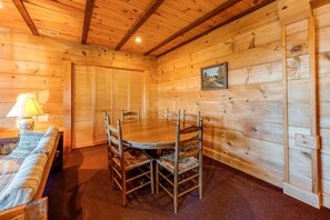 A wooden interior with a round table and chairs, a sofa, and a lamp. - Dog-friendly, Lake View Cabin w/ Furnished Decks, Ping-pong & Darts (Louisa)