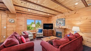 A log cabin interior with a fireplace, television, and red upholstered furniture. - Dog-friendly, Lake View Cabin w/ Furnished Decks, Ping-pong & Darts (Louisa)