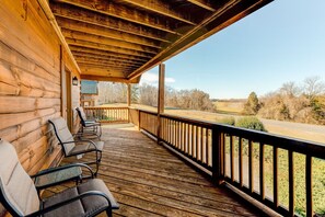 A wooden porch with chairs and a view of a road and trees. - Dog-friendly, Lake View Cabin w/ Furnished Decks, Ping-pong & Darts (Louisa)