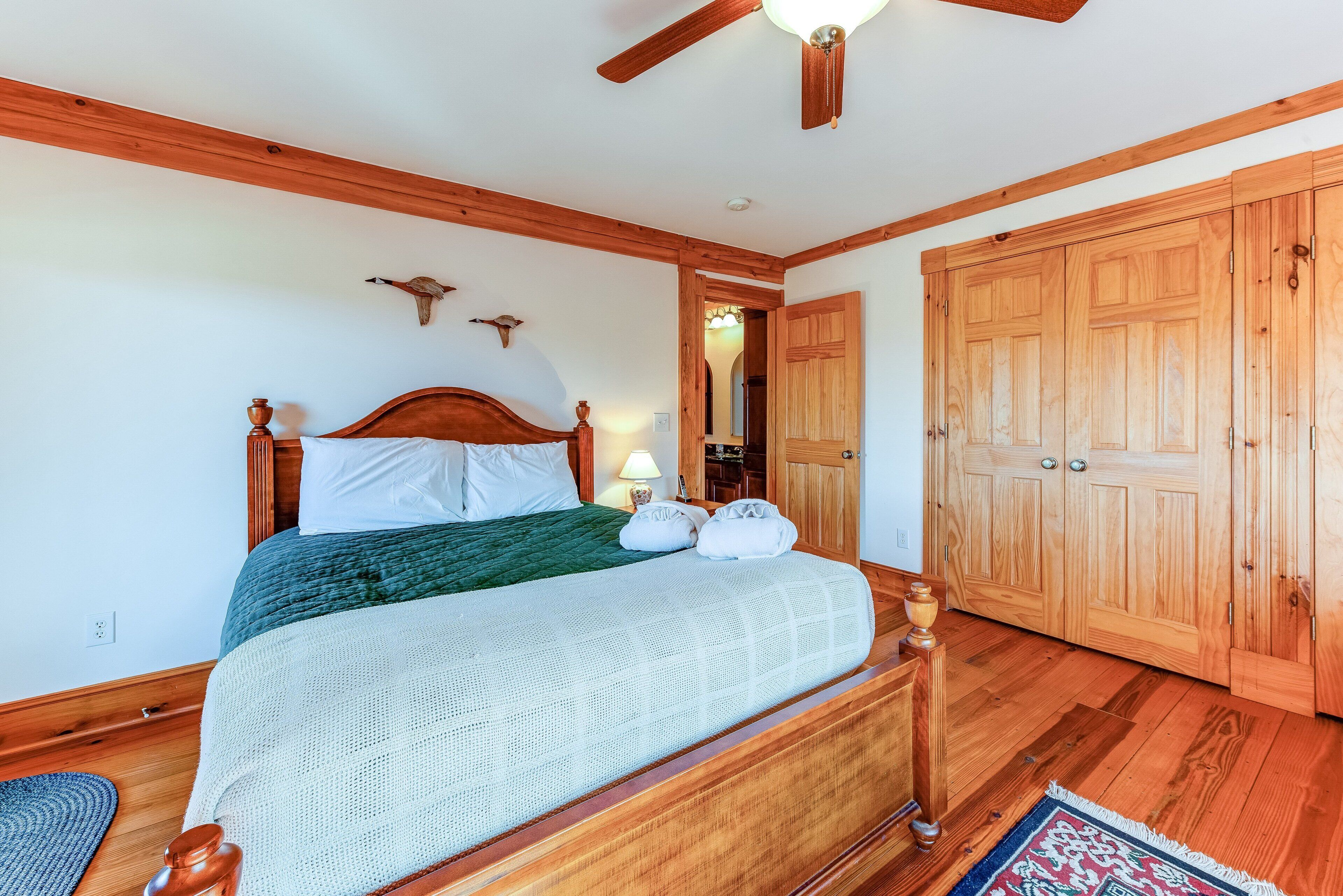 A bedroom with a wooden bed, a ceiling fan, a wooden wardrobe, and a nightstand with a lamp.