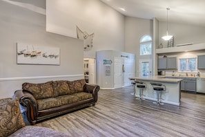 A spacious living room with a large brown patterned sofa, a kitchen with a bar area, and a dining area. - Dog-friendly Home With Free Wifi, Central AC, Firepit, & Furnished Deck (Mineral)