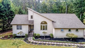 A two-story house with a sloped roof, a front porch, and a landscaped yard with various shrubs and a small tree. - Dog-friendly Home With Free Wifi, Central AC, Firepit, & Furnished Deck (Mineral)
