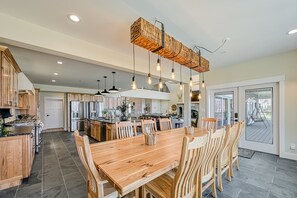 A spacious kitchen with a wooden dining table, hanging light fixtures, and a view to the outside.