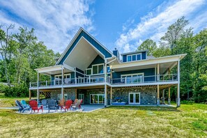 A two-story house with a covered patio, outdoor seating, and a stone facade. - Dog-friendly Lakefront Home With a Game Room, Children's Items, and Firepit (Mineral)
