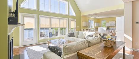 A spacious living area with a high ceiling, large windows, a wooden dining table, and a cozy seating arrangement.