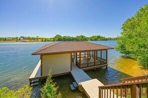 Une maison située au bord de l’eau, dotée d’un patio couvert, d’une petite terrasse et offrant une vue sur un lac.