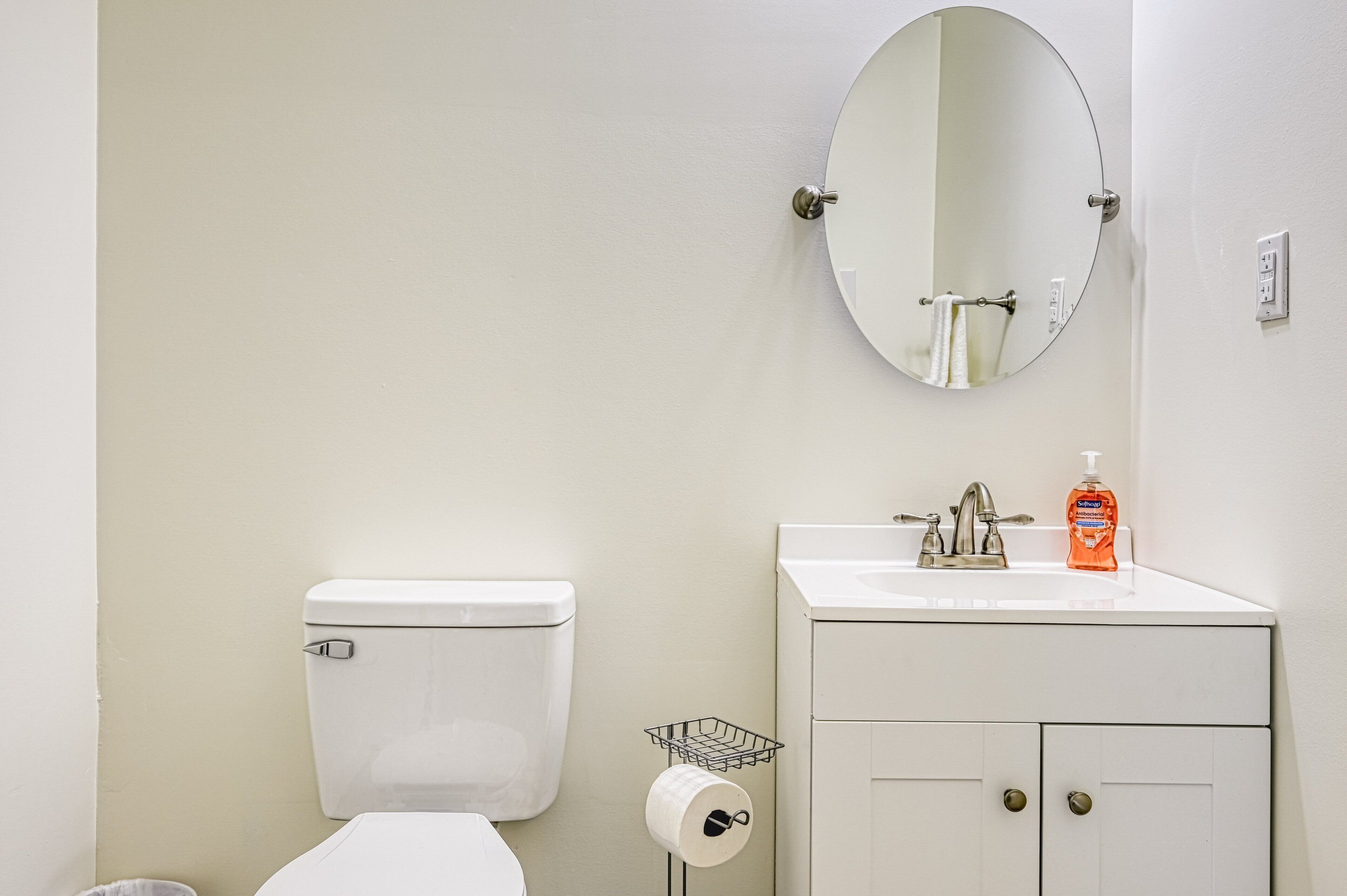 A bathroom with a toilet, sink, mirror, and toilet paper holder.