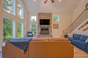 A spacious living room with a stone fireplace, a large TV, and a blue couch. - Dog-friendly Lakefront Home With Dock, Game Room, Kayaks, hot Tub, & Firepit (Mineral)