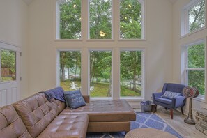 A room with a large window, a brown leather sofa, a blue armchair, and a vintage fan. - Dog-friendly Lakefront Home With Dock, Game Room, Kayaks, hot Tub, & Firepit (Mineral)