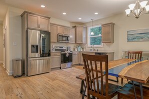 A modern kitchen with stainless steel appliances, wooden cabinets, and a dining area with a glass table and chairs.