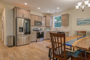 Una cocina moderna con electrodomésticos de acero inoxidable, armarios de madera y un comedor con mesa y sillas de vidrio.