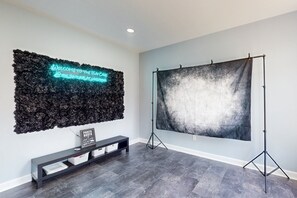 A room with a dark wood floor, a black bench, a neon sign, and a large photo booth backdrop. - Dog-friendly Spacious House W/private Pool, Private Pool Table & Ping Pong Table (Mineral)