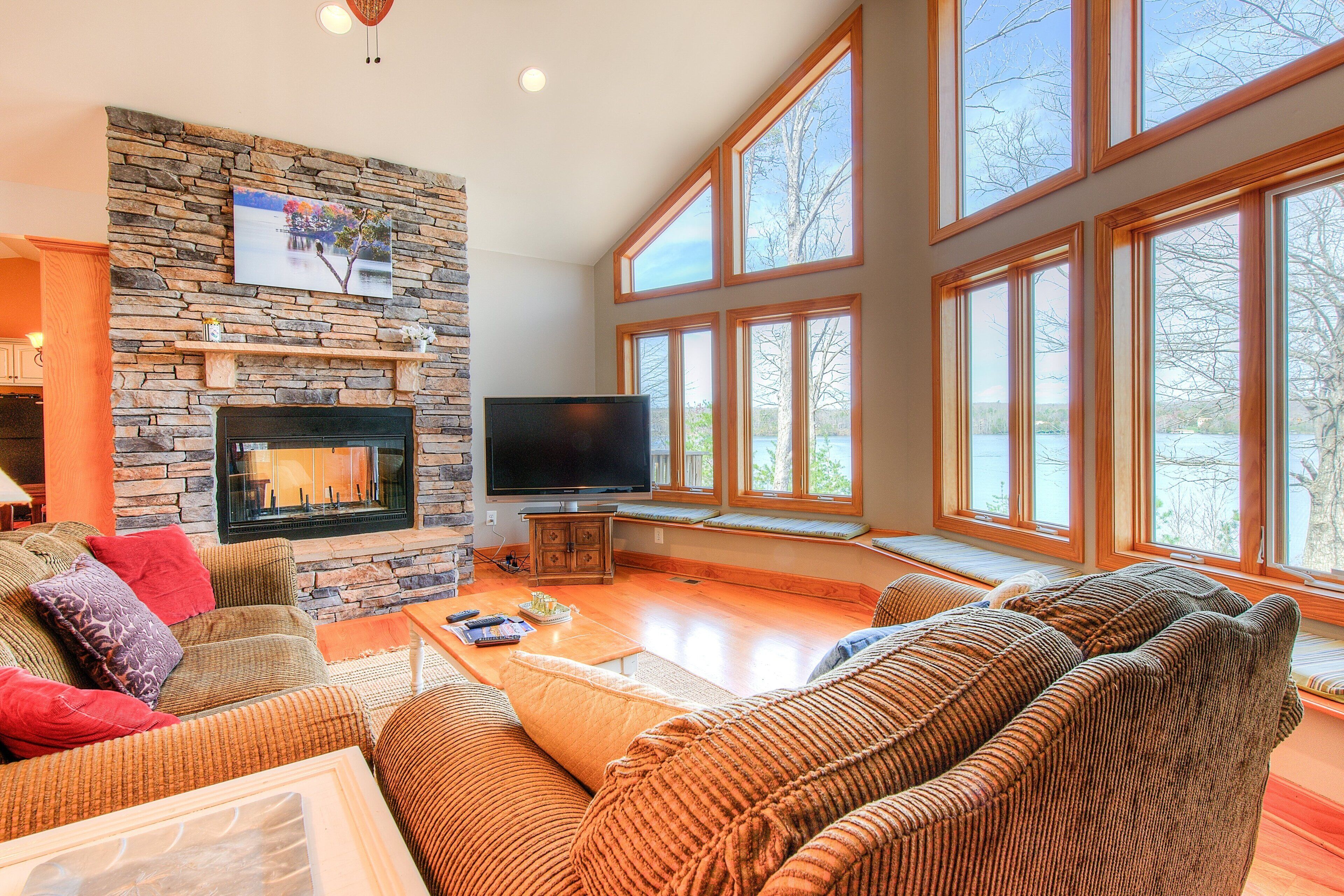 A living room with a stone fireplace, a flat-screen TV, and large windows.
