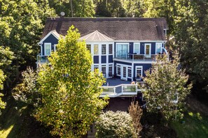 A two-story house with a balcony, surrounded by trees. - Lakefront Home With Private hot Tub, Wifi, fun rec Room, & Beach Area (Mineral)