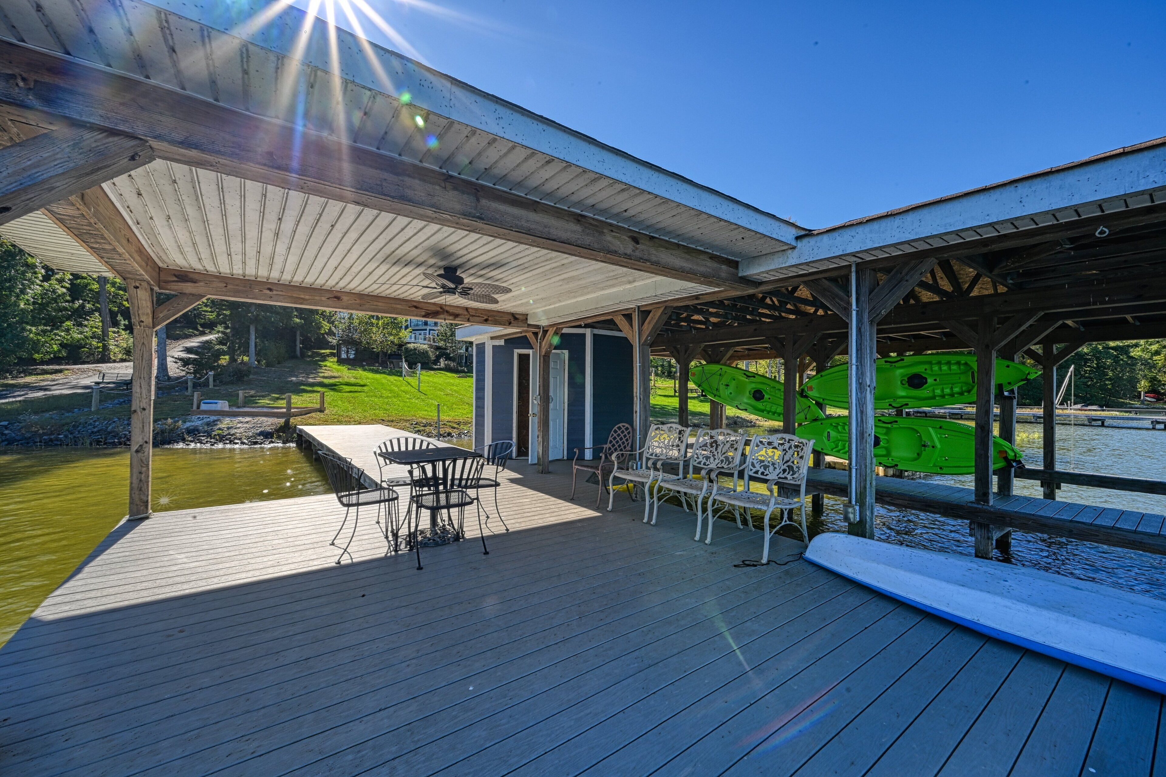 A covered outdoor deck with a table and chairs, a kayak, and a view of a water body.
