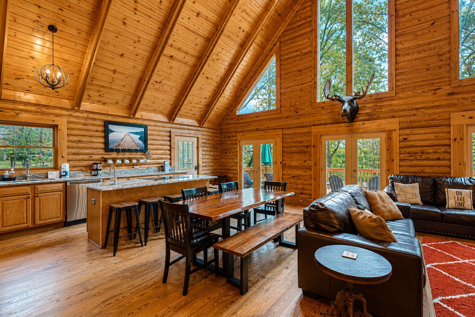 A log cabin interior with a wooden dining area, kitchen, and a living room with a leather sofa.
