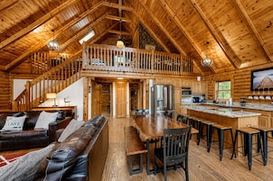 A spacious log cabin with a loft bedroom, a dining area, and a kitchen.