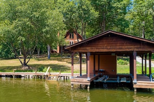A wooden cabin with a dock extending into a lake, surrounded by trees.