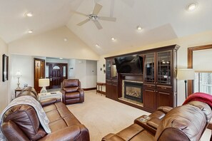 Ein Wohnzimmer mit Ledersofas, einem Kamin, einem Fernseher und einem Deckenventilator.