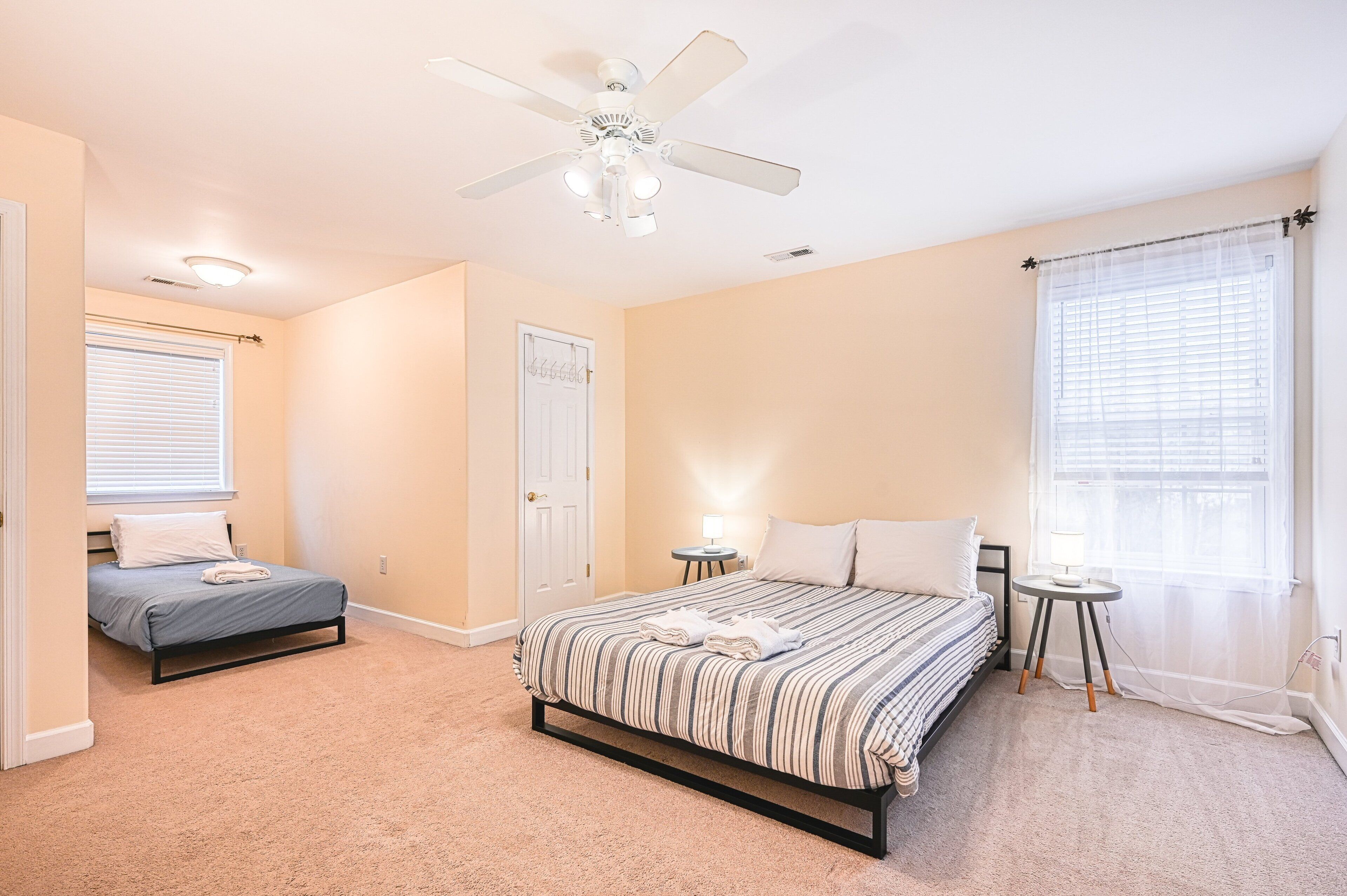 Une chambre à coucher comprenant un lit, un petit lit, un ventilateur de plafond, une fenêtre avec des stores et une porte.