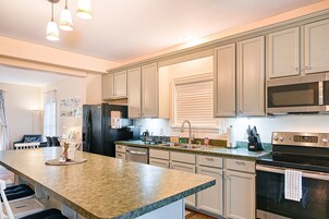 Una cocina con encimera de granito, electrodomésticos de acero inoxidable, armarios blancos e iluminación colgante.