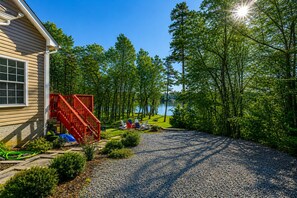 A house with a gravel driveway, a red staircase, and a view of a lake surrounded by trees. - Lakeside Retreat With a Firepit, Dock, Deck, hot Tub, Pool Table - dog Friendly (Orange)