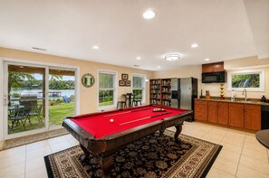 Une table de billard dans une pièce comprenant une cuisine, un coin repas et donnant sur un lac.