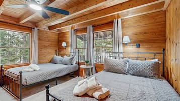 A wooden cabin bedroom with two beds, a ceiling fan, and large windows.