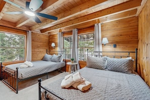 A wooden cabin bedroom with two beds, a ceiling fan, and large windows. - Relaxing Lakeside Cabin With Private Dock, Firepit, Boat Ramp and Water Access (Bumpass)